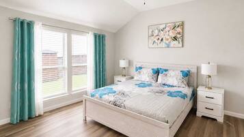 Een slaapkamer met een bed, twee nachtkastjes, een plafondventilator, een raam met gordijnen en een aan de muur hangend schilderij.