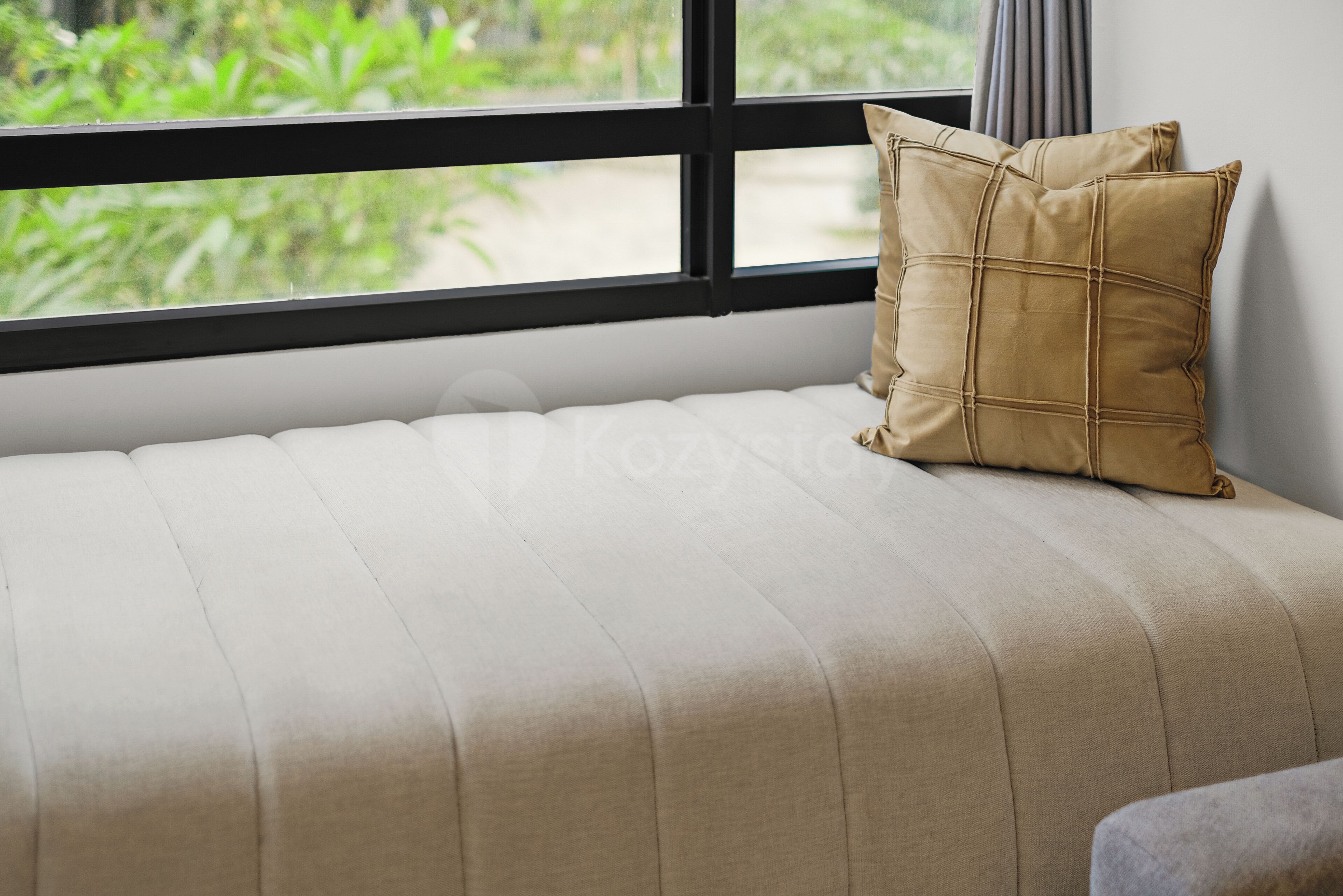 A sofa with a cushion, a window with a view of greenery, and a wall.
