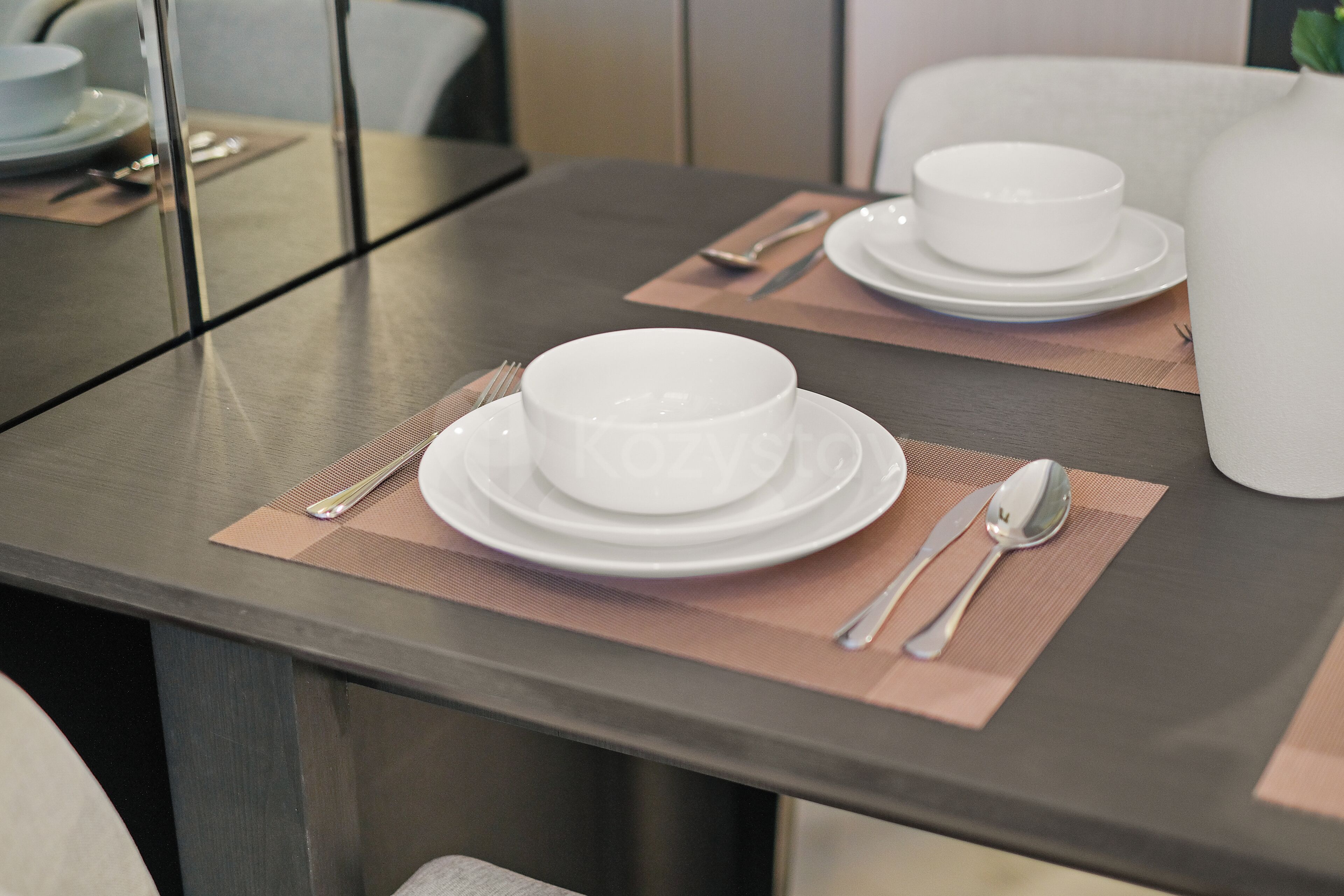 Mesa de comedor con platos blancos, cubiertos y un bol para dos comensales.