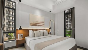 Un dormitorio moderno con una cama grande, una mesita de noche, una lámpara de lectura, un cuadro enmarcado y vistas de edificios por la ventana.