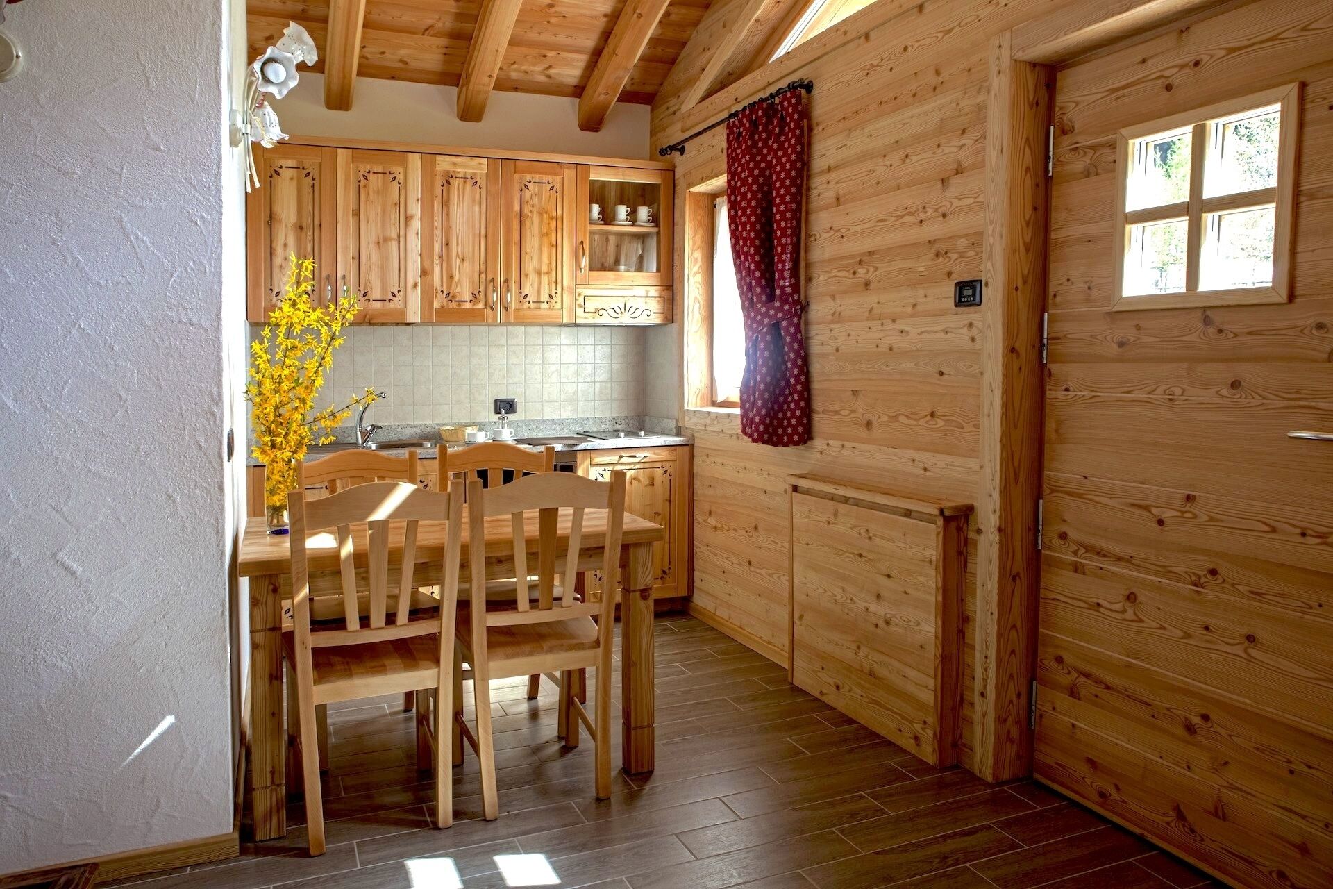 Interior de madera con cocina, comedor y una puerta con ventanal.