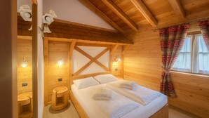 Een slaapkamer in een houten chalet, met een bed, nachtlampjes en een raam met gordijnen.