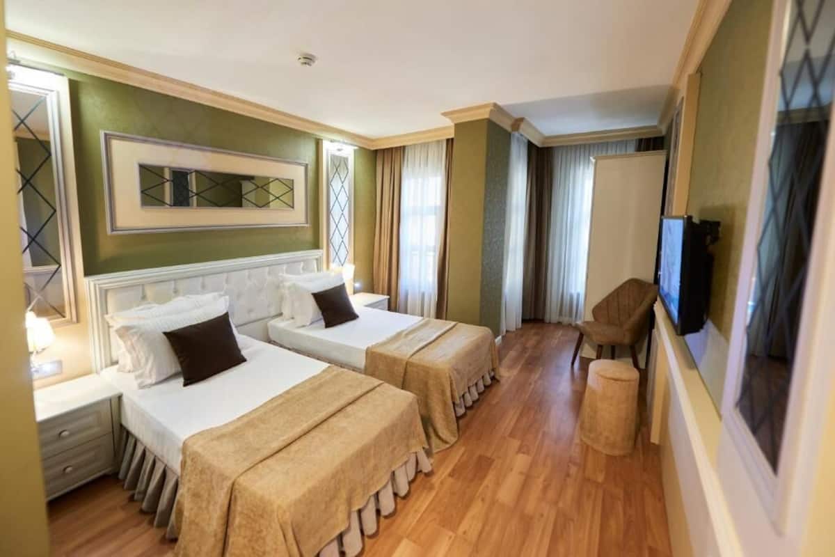 A hotel room with two beds, a television, a chair, and a small stool.