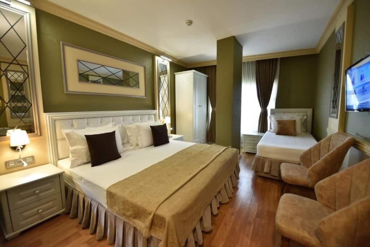 A hotel room with a large bed, a smaller bed, a desk, a chair, and a TV.