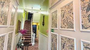 A hallway with patterned wallpaper, a chandelier, a staircase, and a fire extinguisher.