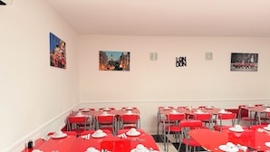 A dining area with red tables and chairs, white table settings, and wall art depicting cityscapes.