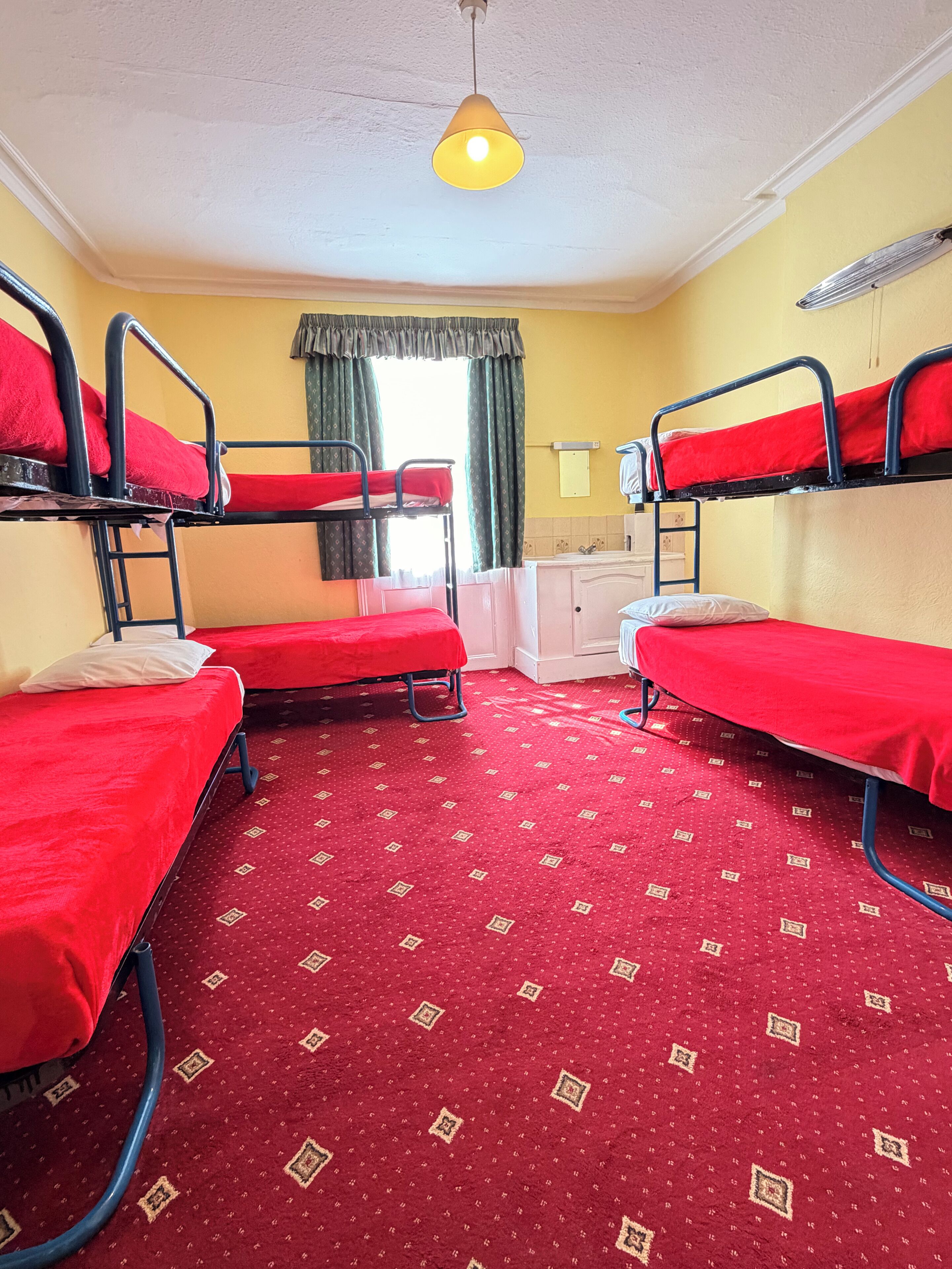 Une chambre avec des lits superposés, une moquette à motifs, une fenêtre avec des rideaux et un luminaire suspendu.