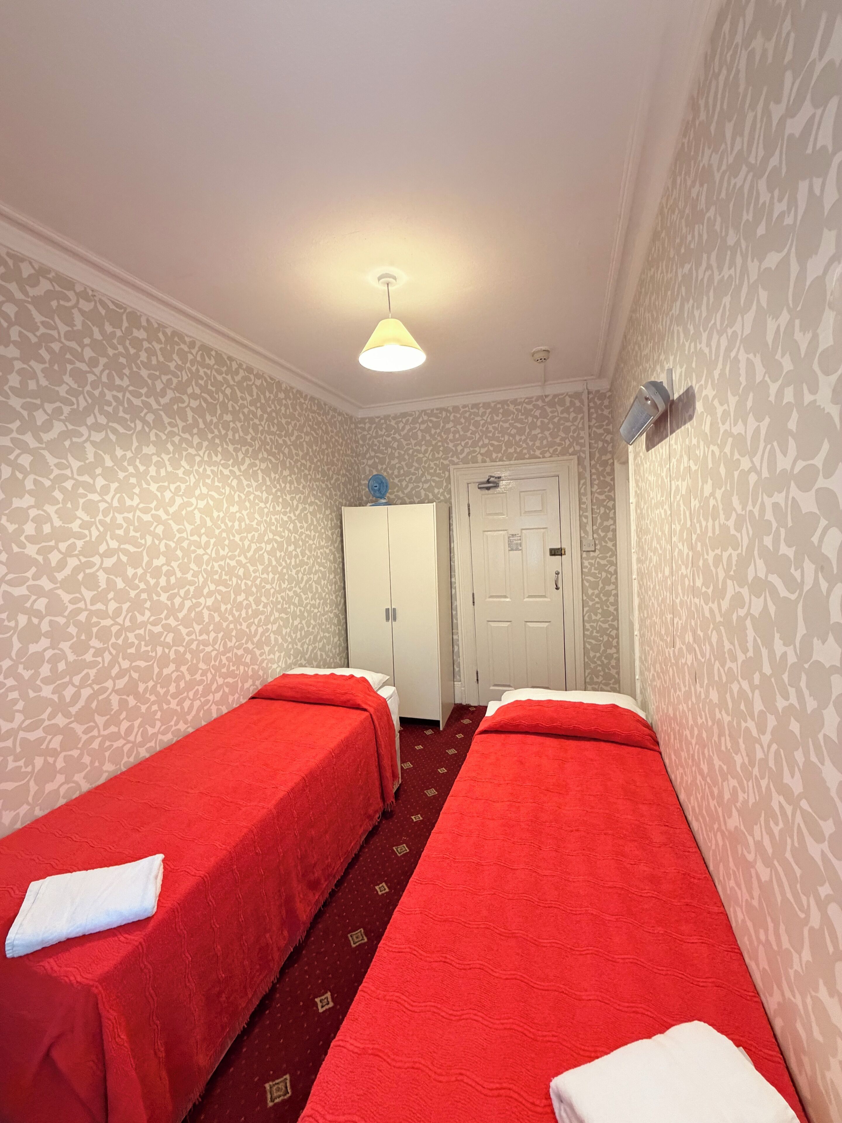 A room with two single beds, a wardrobe, a door, and a patterned wallpaper.