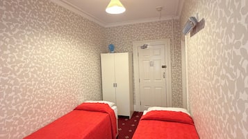 A room with two single beds, a wardrobe, a door, and a patterned wallpaper.