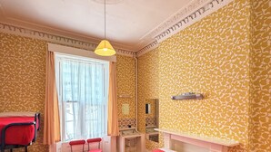 A hotel room with two beds, a desk, a chair, a window with curtains, and a patterned wall.