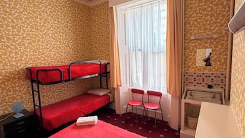 A room with a bunk bed, a desk, a chair, a window with curtains, and a radiator.