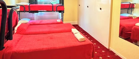 A hotel room with two red beds, a mirror, a wardrobe, and a window with curtains.