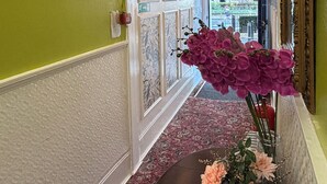 A hallway with a clock, a vase with flowers, and a patterned carpet.