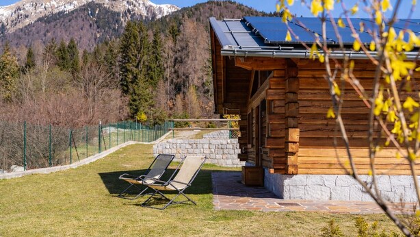 A log cabin with a stone foundation, a solar panel roof, and a clear view of a snow-capped mountain in the background. - Chalet Eco-Lodge Faè - Garden Chalet (Sant'Antonio di Mavignola)