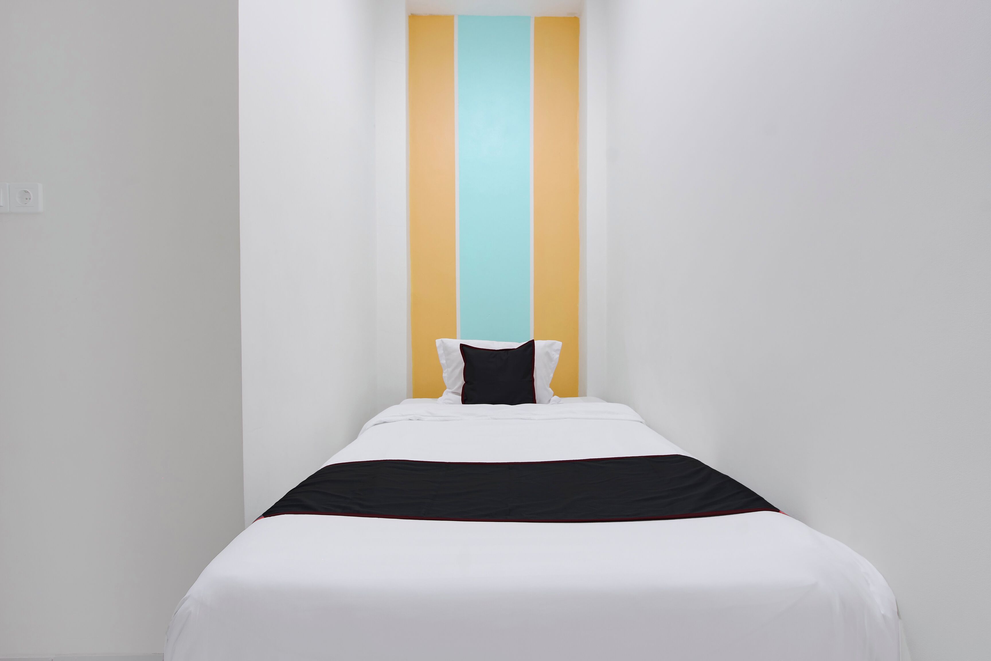 A single bed with white bedding, a black and red accent, and a pillow.