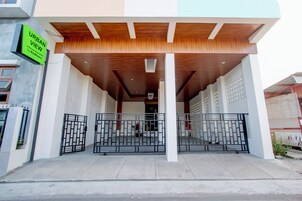 Entrada de un edificio moderno con un vestíbulo cubierto, puertas metálicas y un letrero que dice 'URBAN VIEW by Red Decorz'.