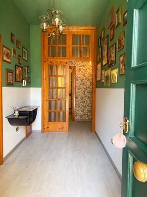 A hallway with a wooden door, a black shelf with a vase, and a chandelier.