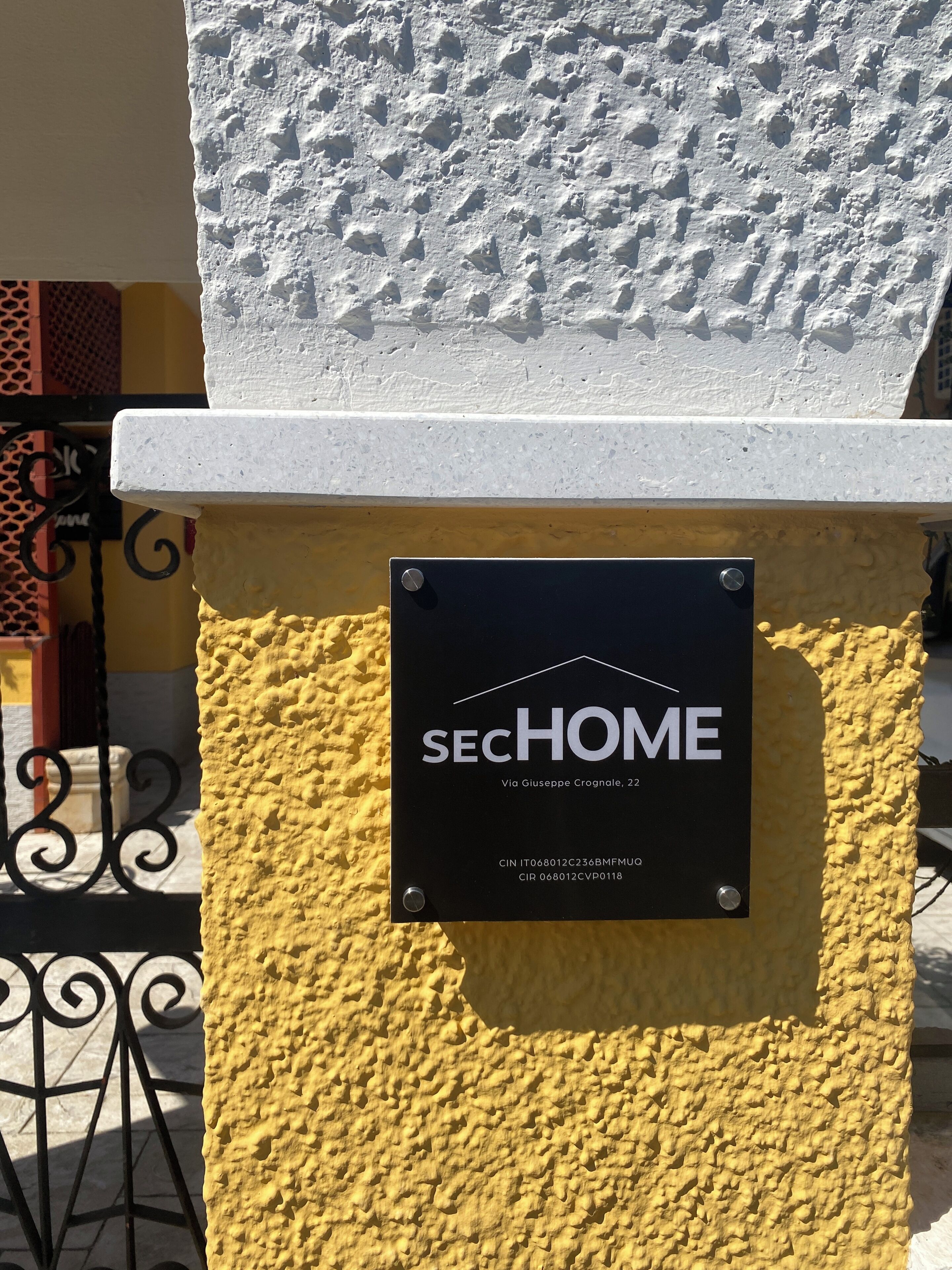 Ein Schild mit 'SECHOME' und Adressangaben an einer strukturierten gelben Wand.