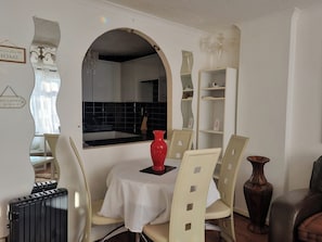 Comedor con una mesa, sillas, un florero rojo y una cocina al fondo.