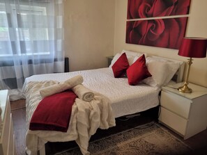 Una cama bien hecha con ropa de cama blanca, almohadas rojas y una manta roja, además de un albornoz blanco a un lado.