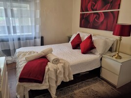Uma cama bem arrumada com roupa de cama branca e almofadas vermelhas, um cobertor vermelho e um roupão branco ao lado.