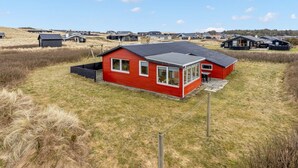 A red house with a large window, surrounded by a grassy field and other houses in the background. - "Myra" - 100m from the sea by Interhome (Løkken)