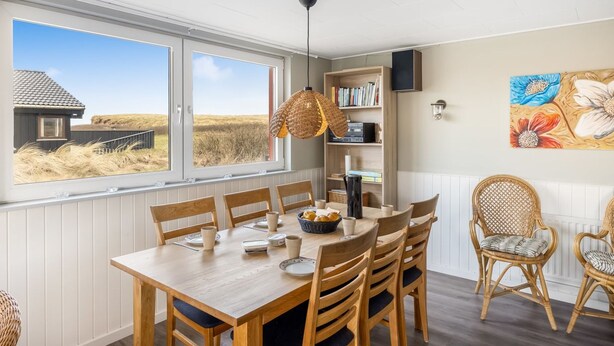 A dining area with a wooden table, chairs, a hanging light fixture, a bookshelf, and a window with a view of the landscape. - "Myra" - 100m from the sea by Interhome (Løkken)