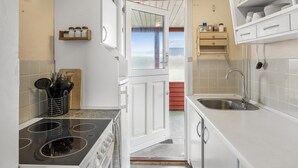 A compact kitchen with white cabinets, a stove, a sink, and a window with a view. - "Myra" - 100m from the sea by Interhome (Løkken)