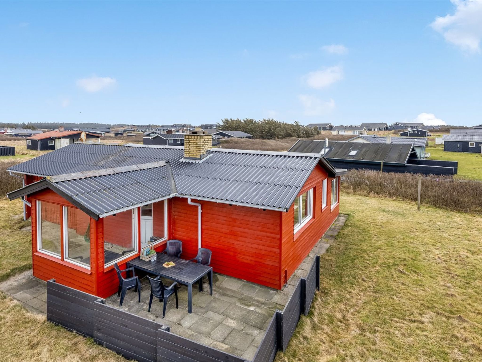 Une maison mobile rouge avec une terrasse, une petite table et des chaises.