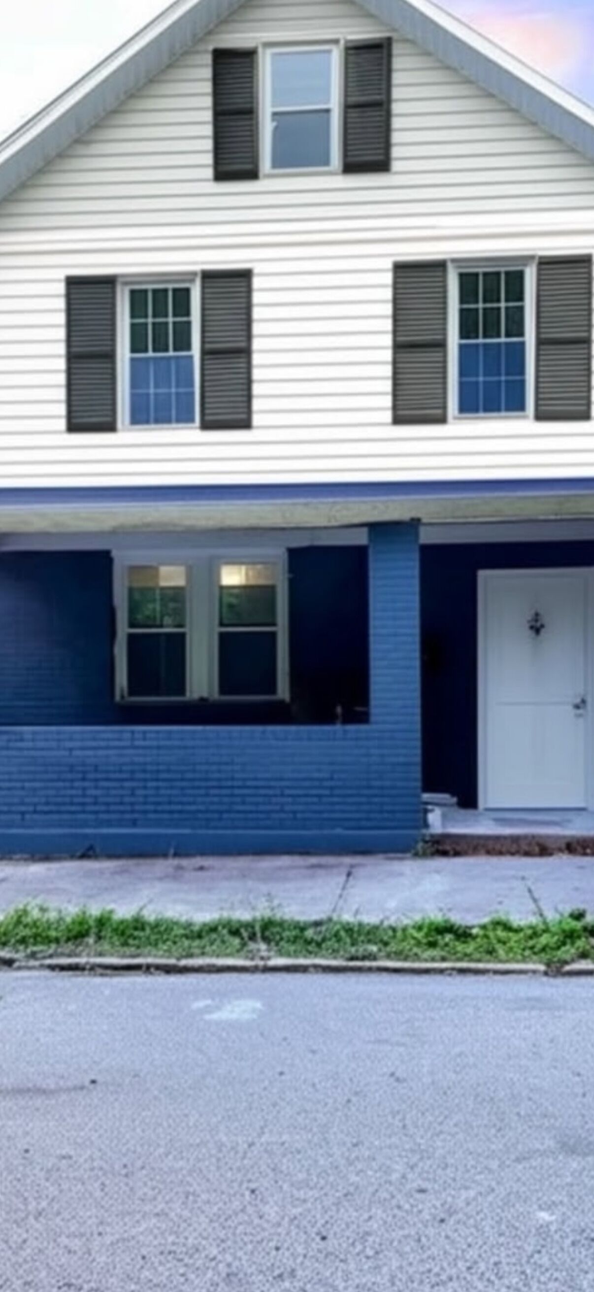 A two-story house with a front porch, a garage door, and a driveway.