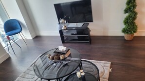 Een woonkamer met een televisie, een glazen salontafel, een blauwe stoel en een potplant.