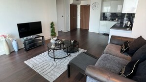 Een moderne woonkamer met een flatscreen televisie, een bank, een salontafel en een keuken op de achtergrond.