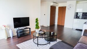 A modern living room with a flat-screen TV, a glass coffee table, and a small potted plant. - Cozy London Apartment With 2 Bedrooms (London)