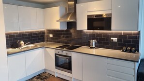 Een moderne keuken met witte kastjes, een zwart betegelde achterwand, roestvrijstalen apparatuur en een inbouwoven.