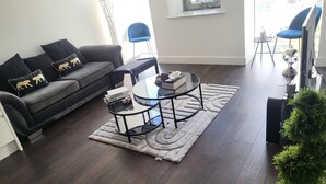 A living room with a dark wood floor, a black sofa with leopard print cushions, a glass coffee table, and a small round table with a globe. - Cozy London Apartment With 2 Bedrooms (London)
