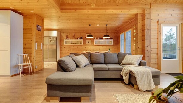 Ein modernes Blockhaus-Interieur mit einem Ecksofa, einem kleinen weißen Sessel und integrierten Regalen.
