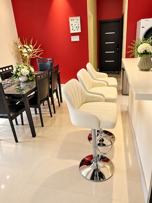 A modern kitchen with a red accent wall, a dining area with a marble table, and a bar stool. - Peaceful Hilltop Retreat/Ocho Rios/Community Pool (Ocho Rios)