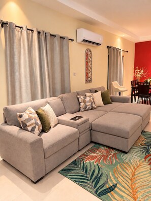 A modern living room with a sectional sofa, a dining area, and an air conditioning unit. - Peaceful Hilltop Retreat/Ocho Rios/Community Pool (Ocho Rios)