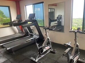 A gym with treadmills and stationary bikes, large windows, and a view of greenery. - Peaceful Hilltop Retreat/Ocho Rios/Community Pool (Ocho Rios)