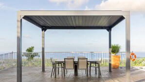 A covered outdoor seating area with a table and chairs, a potted plant, and a lifebuoy on a terrace with a view. - Peaceful Hilltop Retreat/Ocho Rios/Community Pool (Ocho Rios)