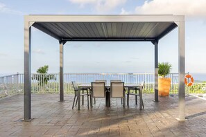 A covered outdoor seating area with a table and chairs, a potted plant, and a lifebuoy on a terrace with a view. - Peaceful Hilltop Retreat/Ocho Rios/Community Pool (Ocho Rios)
