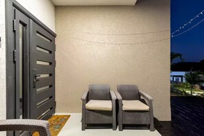 A patio area with two wicker chairs and a table, a textured wall, and a partially visible door. - Peaceful Hilltop Retreat/Ocho Rios/Community Pool (Ocho Rios)