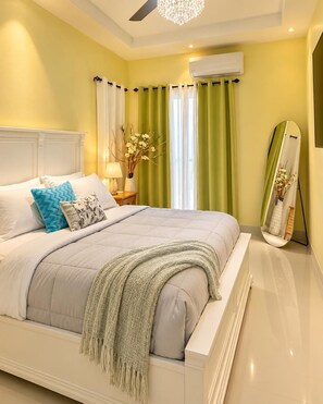 A bedroom with a bed, nightstand, lamp, air conditioning unit, and a mirror. - Peaceful Hilltop Retreat/Ocho Rios/Community Pool (Ocho Rios)