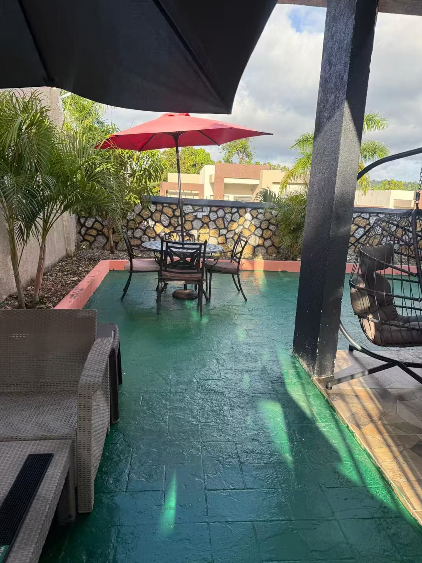 An outdoor patio with a stone wall, a red umbrella, and a table with chairs.