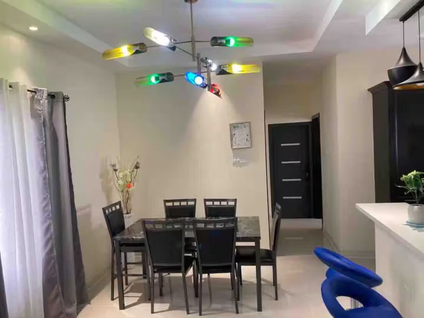 A dining area with a table and chairs, a ceiling fan with lights, a door, and a plant.