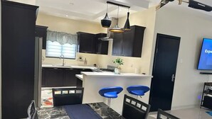 A modern kitchen with dark cabinetry, a white countertop, and two blue bar stools. - Peaceful Hilltop Retreat/Ocho Rios/Community Pool (Ocho Rios)