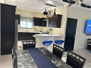 A modern kitchen with dark cabinetry, a white countertop, and two blue bar stools. - Peaceful Hilltop Retreat/Ocho Rios/Community Pool (Ocho Rios)