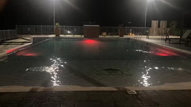 A nighttime swimming pool with two light poles, a wooden deck, and a metal railing. - Peaceful Hilltop Retreat/Ocho Rios/Community Pool (Ocho Rios)