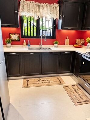 A kitchen with dark cabinets, a white countertop, a sink, and a window with a decorative curtain. - Peaceful Hilltop Retreat/Ocho Rios/Community Pool (Ocho Rios)