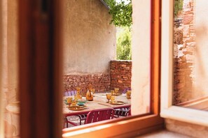 Un espacio de comedor al aire libre con una pared de piedra y una mesa de madera dispuesta con vajilla dorada.